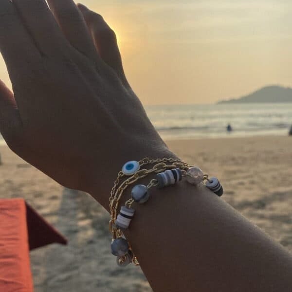 Evil Eye bracelet with blue charm, worn on a hand at sunset beach scene.
